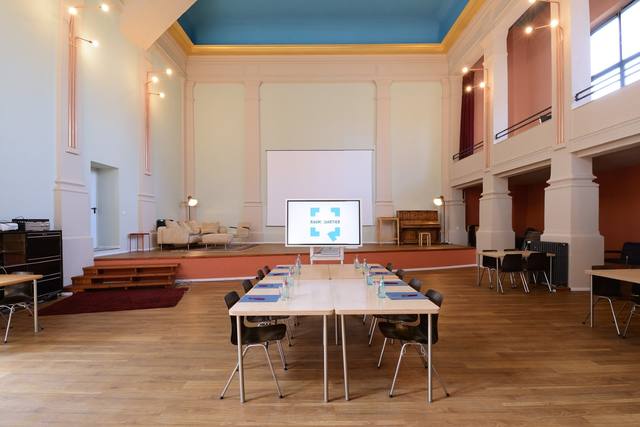 Saal mit Konferenztischen und Bildschirm